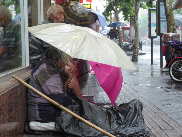 Those without shelter live on the streets as best they can: on this day, trying their best to avoid being soaked by the frequent rain in Shanghai, China while they continue to beg for money.  Photo by Benjamin Clavan, 2015.