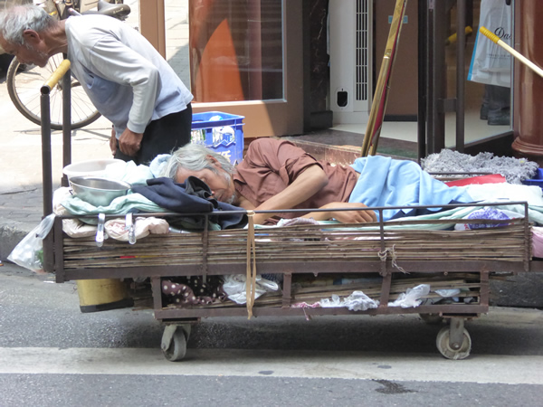 The Shanghai, China home for this double-amputee is a cart, pulled by his companion.  The slots underneath are stuffed with the two men’s belongings.  They survive by begging.  Photo by Benjamin Clavan, Shanghai, 2015.